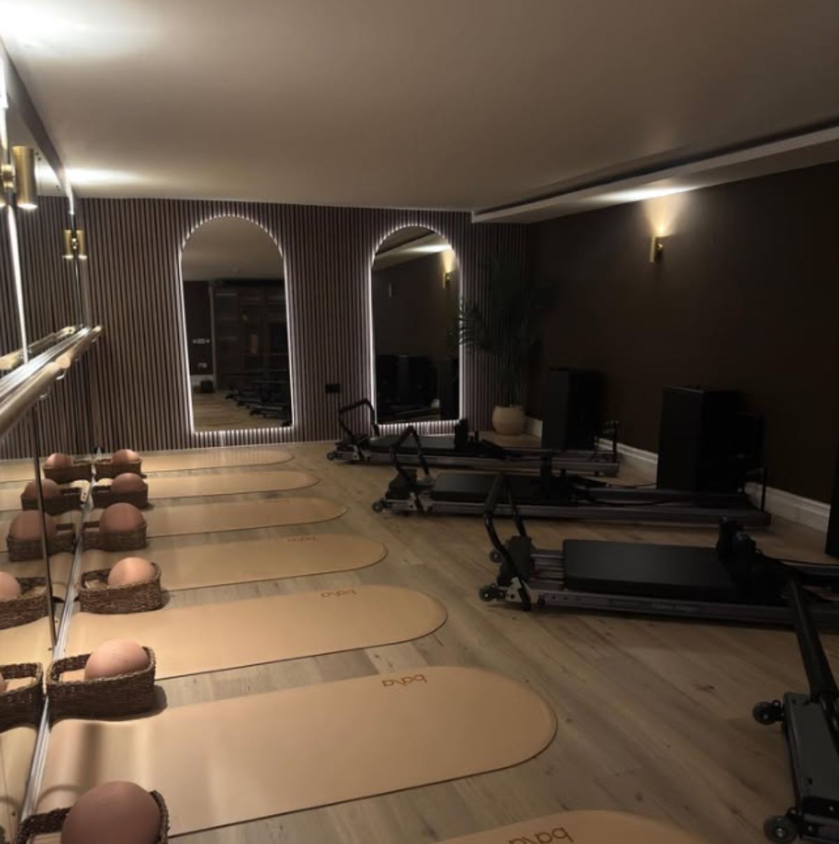 The barre area of the studio, lit slat wall and mirror behind a wooden barre
